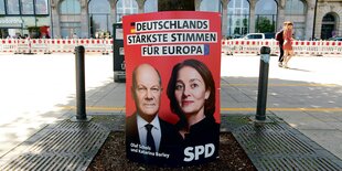 Ein rotes Plakat steht an einem Baum, darauf ein Mann und eine Frau