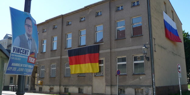 Ein AfD-Wahlplakat, ein Haus mit einer deutschen Flagge und einer russischen Flagge