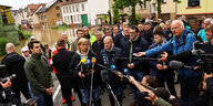 Olaf Scholz und Anke Rehlinger stehen umgeben von einer Menge Journalist:innen vor dem Hintergrund einer überschwemmten Ortsstraße