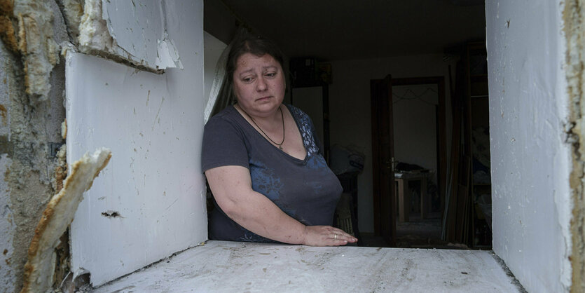 Eine Frau schaut aus dem Fenster eines zerstörten Gebäudes