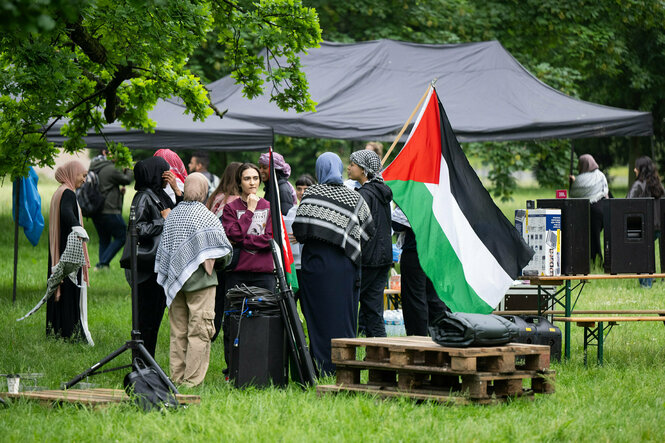 Auf einer Wiese stehen mehrere Aktivist:innen mit Pali-Tüchern und Palästina-Flagge