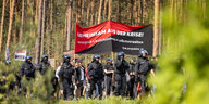 Ein schwarzrotes Banner der Gruppe Perspektive Selbstverwaltung auf der "Wasser Wald Gerechtigkeit" Demonstration in Grünheide 11.5.24, auf dem steht: "Gemeinsam aus der Krise! Enteignen, kollektivieren, selbstverwalten"