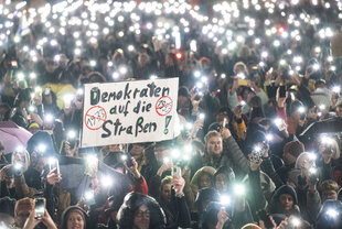 Zu sehen ist eine demonstrierende Menschenmasse mit Protest-Schildern