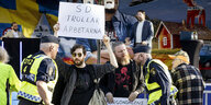 Ein Mann steht vor einer Bühne und hält ein Plakat hoch, auf Schwedisch steht da: "SD trollt die Arbeiter" . Im Hintergrund der rechte Politiker Jimmy Åkesson, im Vordergrund Polizisten.