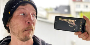 Ein gestelltes Foto von einem Mann, der auf ein Smartphone-Display mit einer Pistole schaut