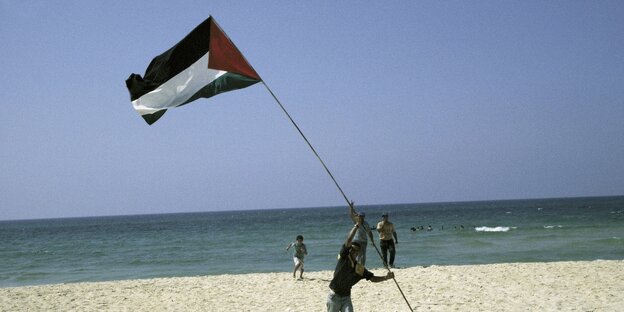 Ein Mann ist an einem Strand am meer und hält eine Palästina-Fahne in den Händen