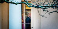 Man sieht Donald Trump im Oval Office durch ein Fenster, hinter einem Vorhang