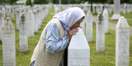 Eine weiß gekleidete Frau küsst einen Grabstein auf einem großen Gräberfeld