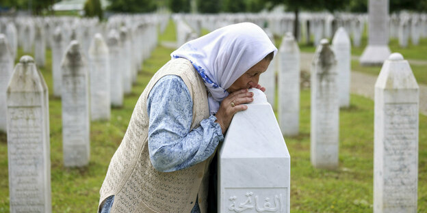 Eine weiß gekleidete Frau küsst einen Grabstein in einer großen Grabstätte