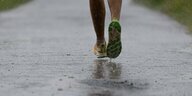 Die Füße eines Joggers, der auf einem regennassen Weg läuft.