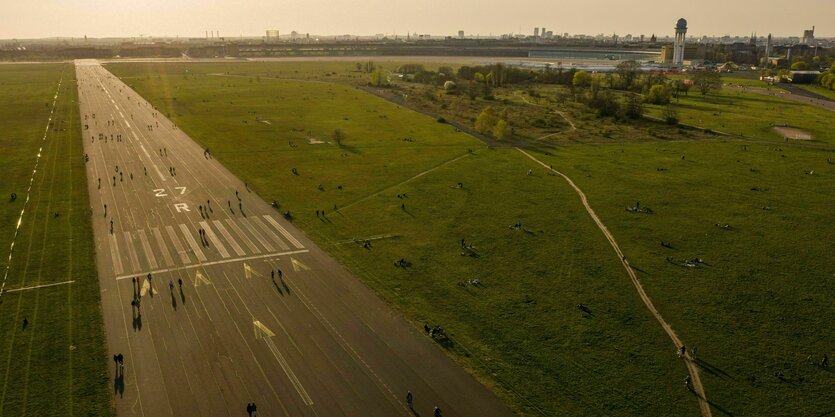 Menschen sind während des Sonnenuntergangs auf dem Tempelhofer Feld unterwegs, im Hintergrund (oben rechts) ist das ehemalige Flughafengebäude zu sehen.