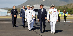 Der französische Präsident Macron, zwei uniformierte Männer und andere Personen auf dem Rollfeld eines Flughafens