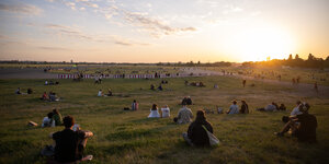 Das Foto zeigt Besucher des Tempelhofer Felds im Gras sitzend in der Abendsonne.