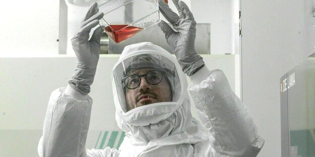Ein Bakteriologe in einem Schutzanzug blickt auf eine Flüssigkeit