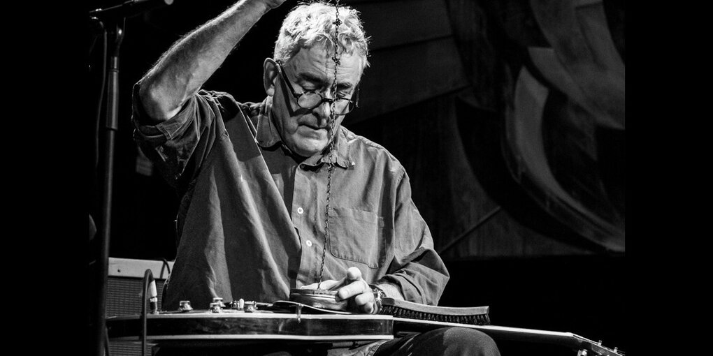 Fred Frith beim experimemtellen Gitarrenspiel, das Instrument liegt auf seinen Beinen