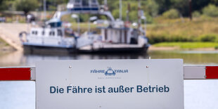 Im Vordergrund sind eine Schranke und ein Schild mit der Aufschrift "Die Fähre ist außer Betrieb" zu sehen, im Hintergrund die Elbe und eine am anderen Flußufer liegende Fähre.