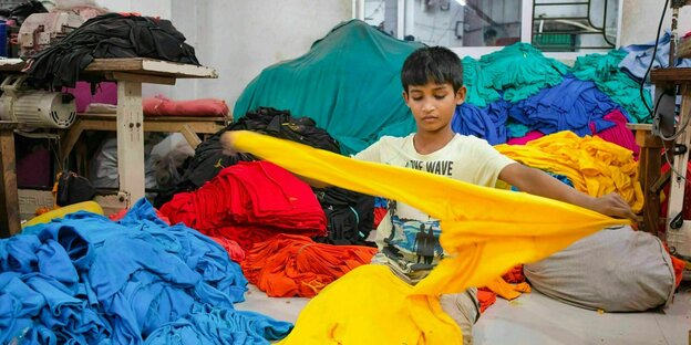 Ein Kind arbeitet in einer örtlichen Bekleidungsfabrik an Kleidungsstücken
