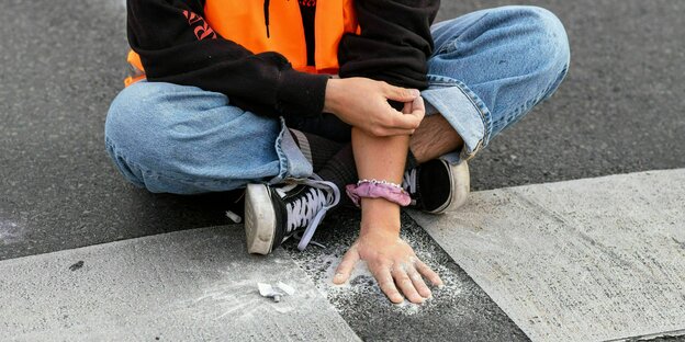 Eine Aktivist klebt mit der Hand am Asphalt fest