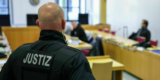 Ein Justizbeamter steht vor drei von sechs Angeklagten