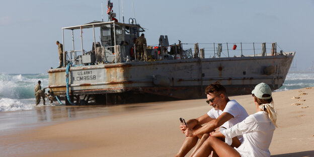 Ein US-Schiff, das Hilfsgüter in den Gazastreifen bringen sollte, ist im israelischen Ashdod gestrandet. Zwei Menschen entspannen sich am Strand davor