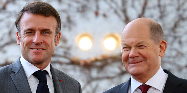 Frankreichs Präsident Macron blinzelt unsicher, Bundeskanzler Olaf Scholz lächelt verlegen