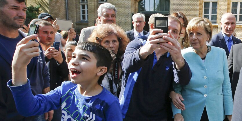 Ein junger Geflüchteter macht ein Selfie von sich und Angela Merkel