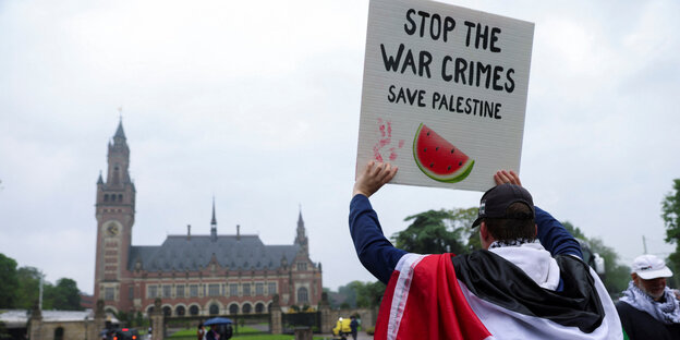 Ein Demonstrant hält vor dem Gebäude des IGH in Den Haag ein Schild hoch, auf dem steht: "Stop the War Crimes. Save Palestine"