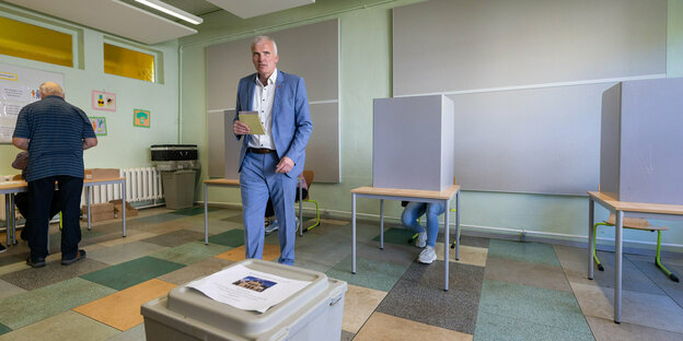 In einem Wahllokal geht ein Mann im hellblauen Anzug auf die Wahlurne zu