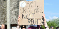Ein Demonstrant hält ein Schild hoch auf dem steht: Sylt: Oben links, nicht rechts