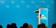 Ein leeres Rednerpult in blau-weiß mit dem Logo der AfD im Hitergrund