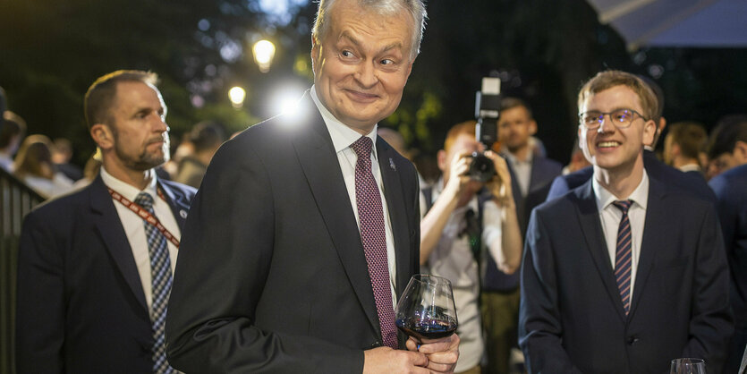 ein Mann mit einem Weinglas in der Hand blickt in Richtung Kamera