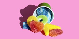 Fruchtgummis in einem Plastikbecher vor rosafarbenem Hintergrund