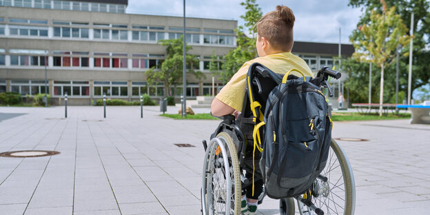 Ein Junge sitzt in einem Rollstuhl vor einem Schulgebäude