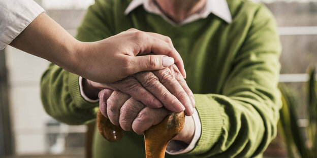 Die Hände einer Pflegerin liegen auf den Händen eines älteres Mannes
