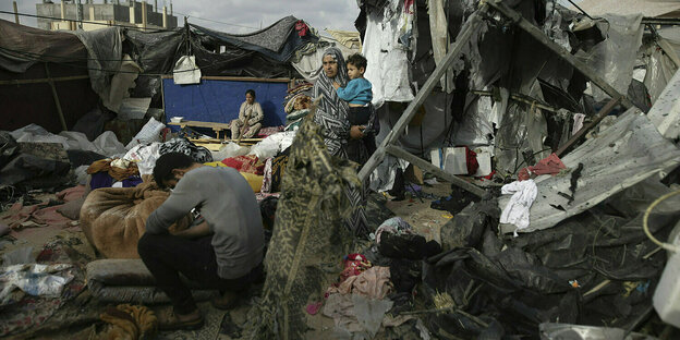 Menschen stehen zwischen den zerstörten Überresten ihrer Zelte