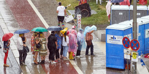 Menschen stehen in einer Kloschlange im Regen