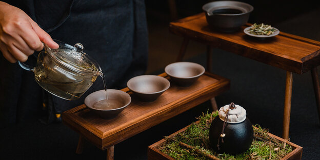 Eine Hand hält eine Teekanne, aus der Tee in Schalen gegossen wird