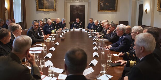 An einem ovalen Konferenztisch sitzt Barack Obama zwischen Militärs