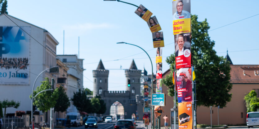 Das Bild zeigt Laternenmasten, die mit Plakaten gesäumt sind.