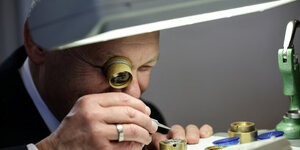 Ein Man inspiziert mit einer Lupe ein Uhrenteil in der Firma Nomos Glashütte.