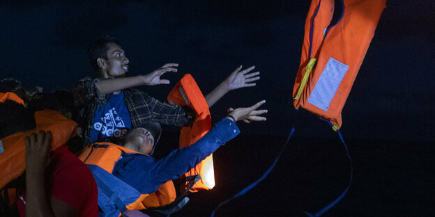 Menschen mit Rettungswesten sind auf einem Boot und warten auf ihre Rettung