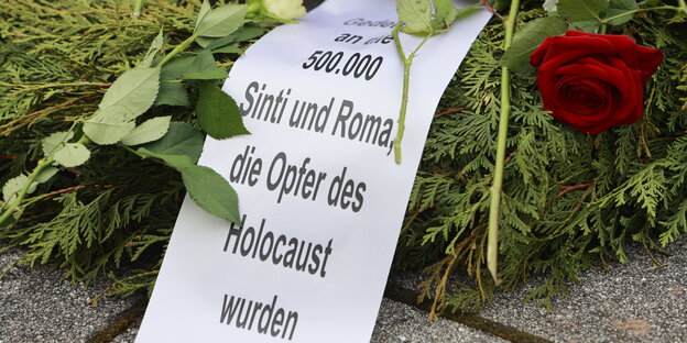 Ein Gedenkranz mit Rosen und einer weißen Schleife mit der Aufschrift "Gedenken an die 500.000 Sinti und Roma, die Opfer des Holocaust wurden".
