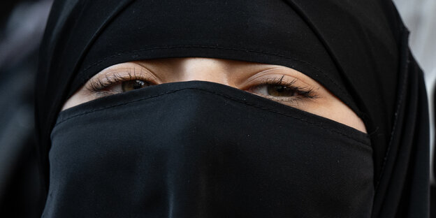 Nahaufnahme einer Frau, die Niqab trägt. Ein Schlitz im schwarzen Stoff zeigt nur die Augenpartie.