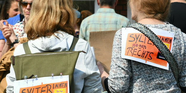 Sylter gegen Rechts!· steht auf Plakaten, die zwei Frauen bei einer Mahnwache am Sonntag auf sylt auf ihre Rücken geheftet haben