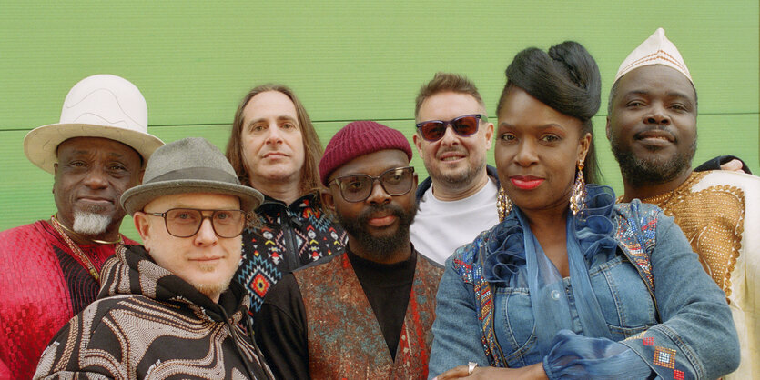 Die MusikerInnen von Ibibio Sound Machine vor einer grünen Wand