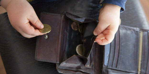 Ein Kind legt eine Münze in ein alte Portmonnaie