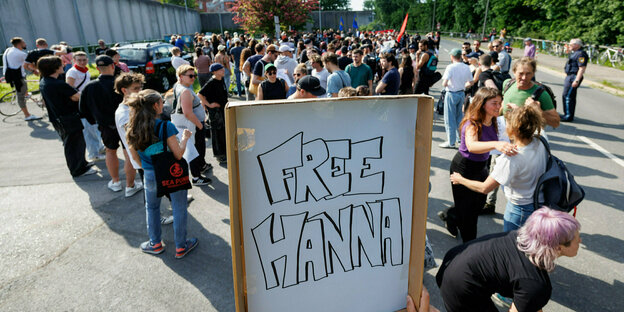 Menschengruppe mit einem Schild "Free Hanna" steht vor einer Gefängnismauer