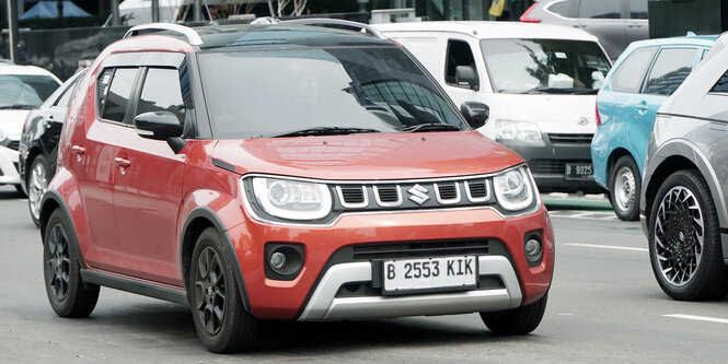 Ein rostroter Suzuki mit indonesischem Kennzeichen fährt zwischen einigen anderen Autos über eine Straße