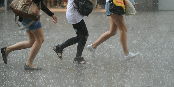 3 Frauen laufen durch den Hagel, der auf Asphalt prasselt