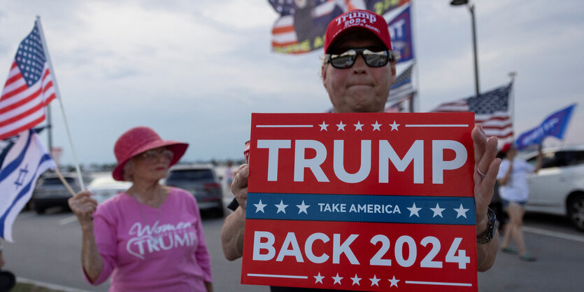 Ein Mann hält ein Plakat mit der Aufschrift "Trump Back 2024" in die Höhe